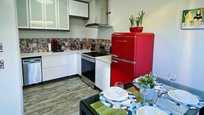 A compact kitchen with white cabinets, a red refrigerator, and a dining area with a glass table set for two.