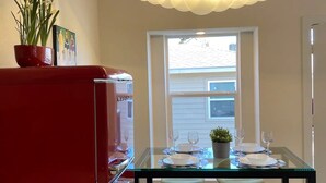 A dining area with a glass table, four wooden stools, and a red cabinet.