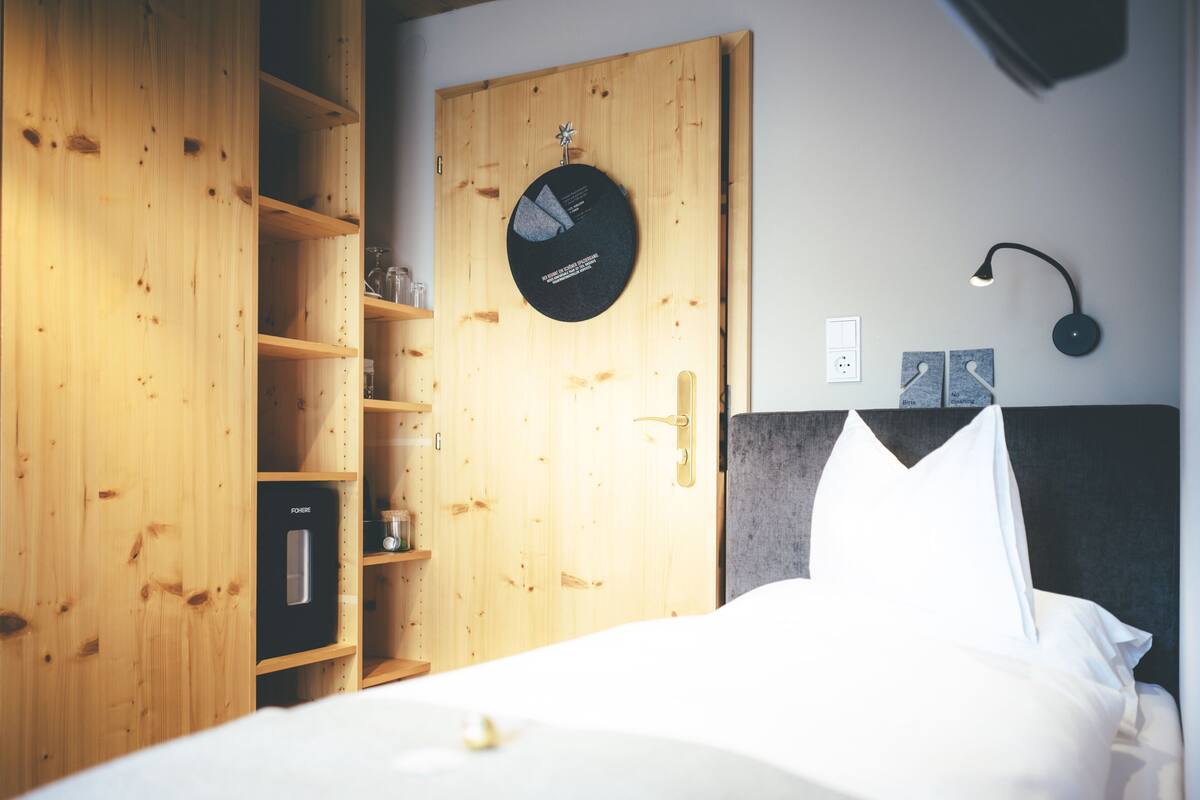A bedroom with a bed, a wooden wardrobe, a round clock, and a bedside table with a lamp.