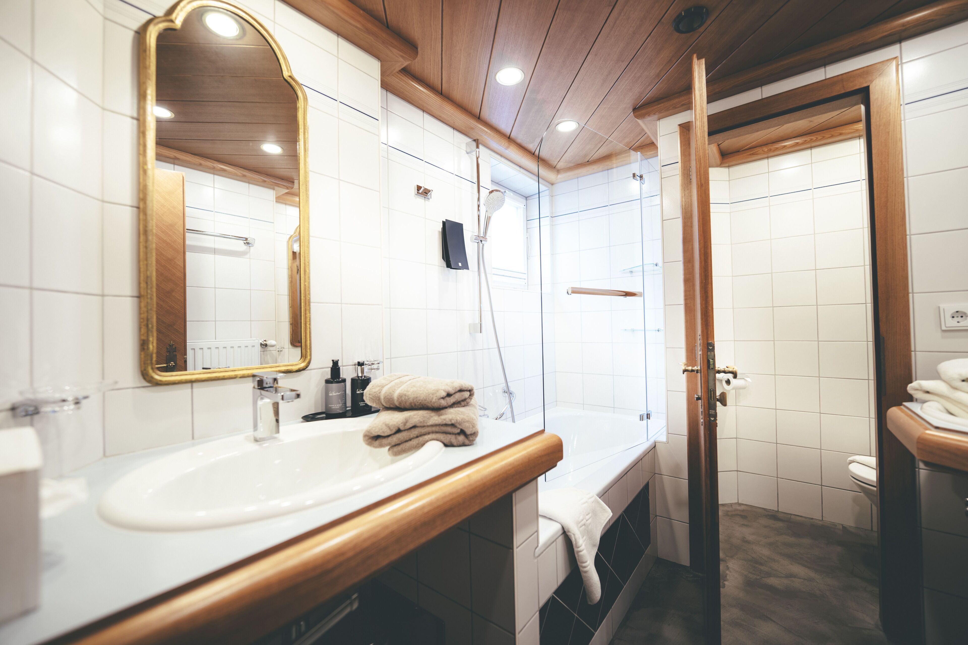 Ein modernes Badezimmer mit Waschtisch aus Holz, einem großen Spiegel, einer Badewanne und einem WC.
