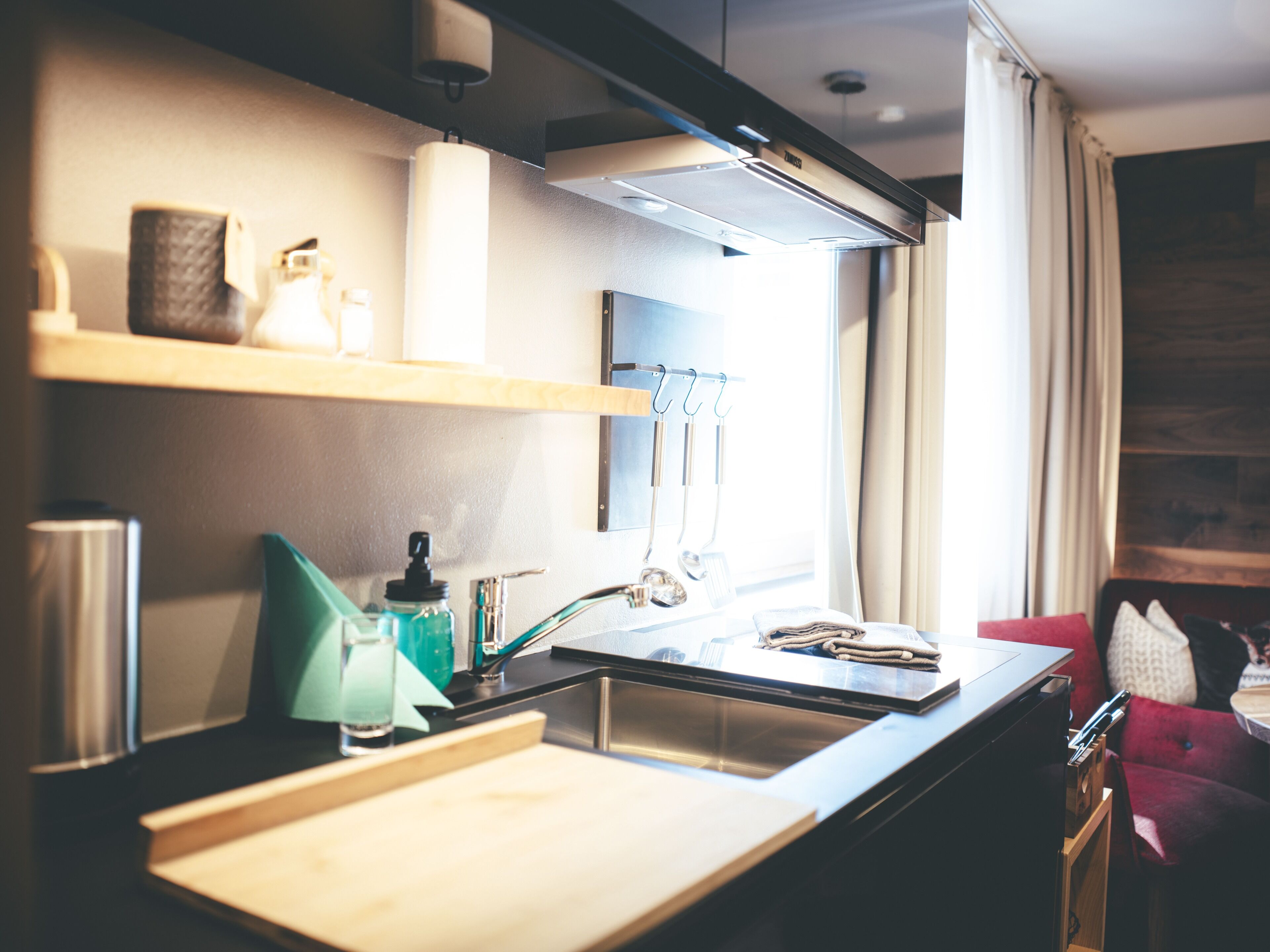 Una cocina moderna con un lavamanos de acero inoxidable, encimera de madera y una ventana con cortinas.