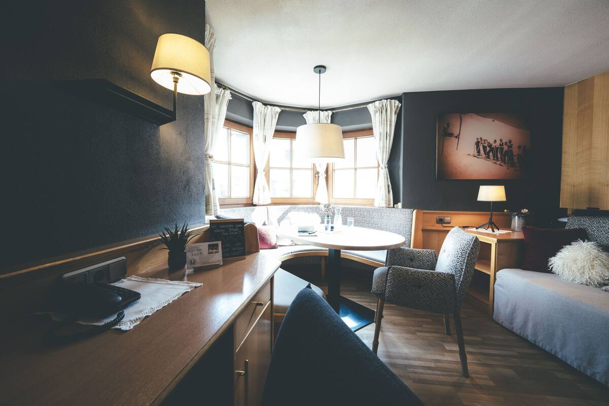 A cozy hotel room with a wooden desk, a round table, a sofa, and a bed.