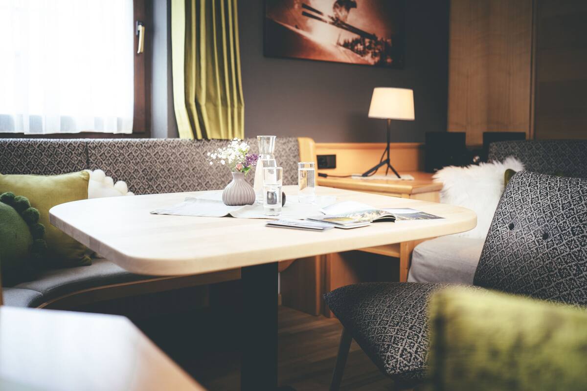 A hotel room with a neatly arranged dining table, a sofa, a lamp, and a painting on the wall.