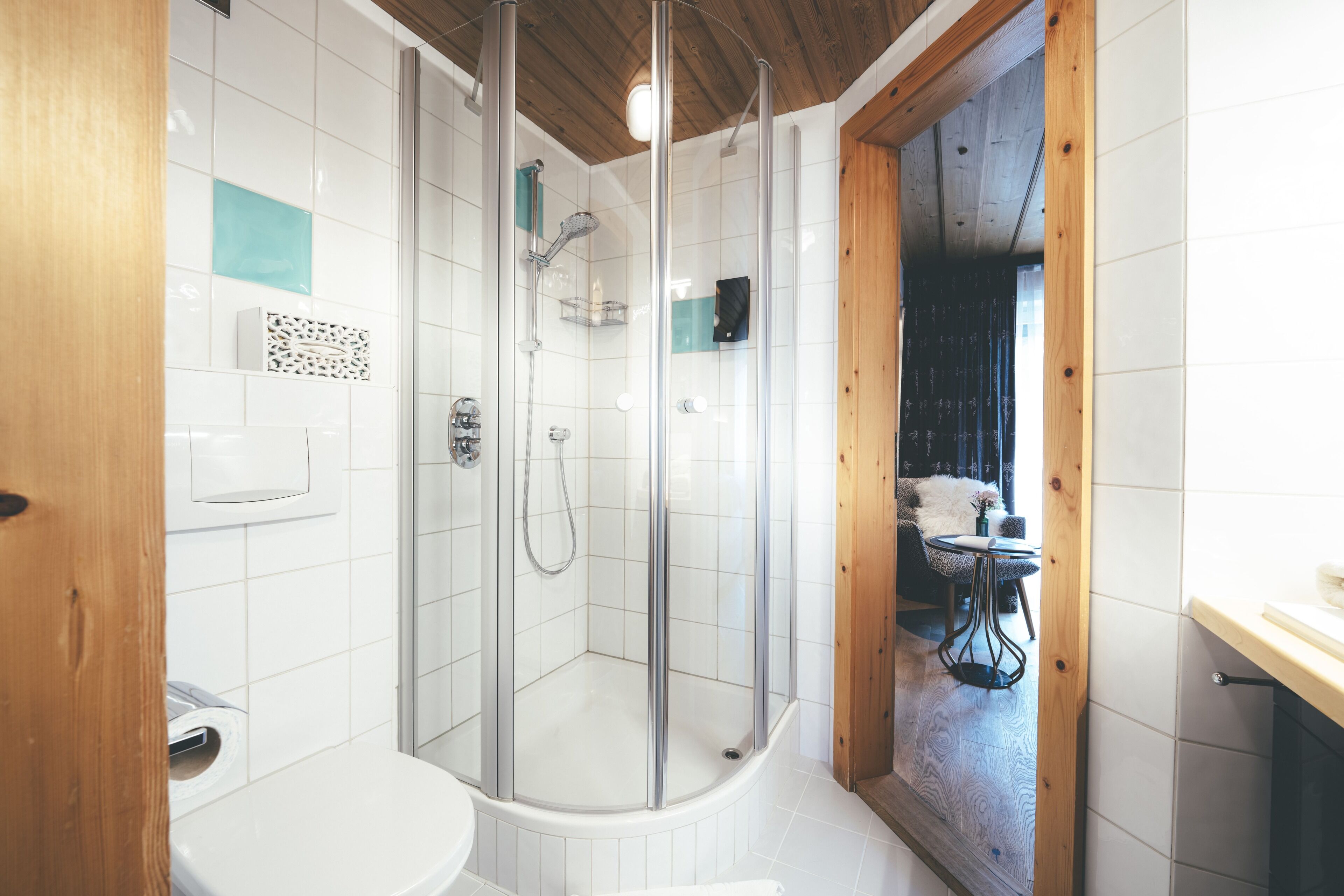 A modern bathroom with a glass-enclosed shower, white tiles, and wooden accents.