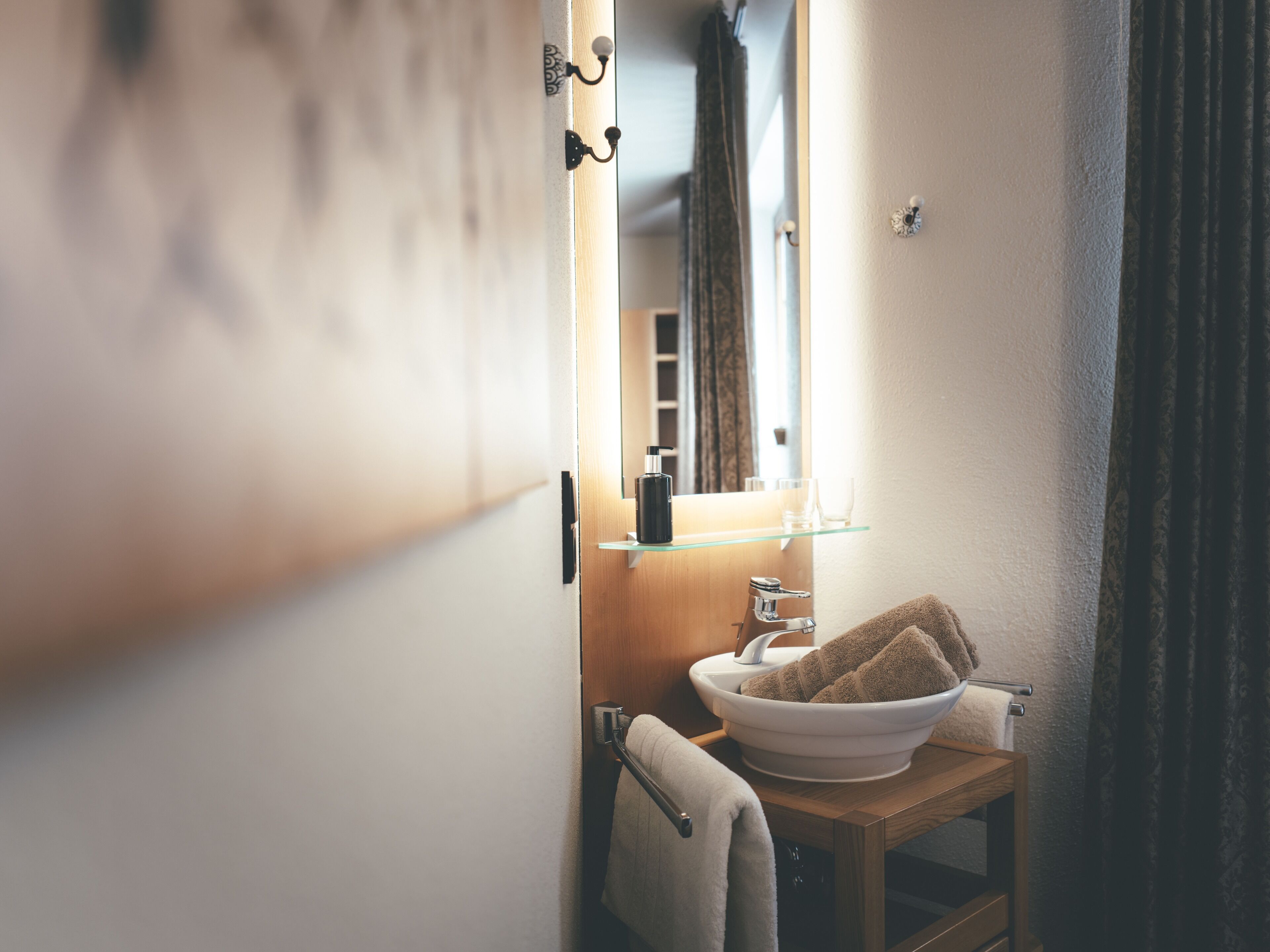 A bathroom with a wooden vanity, a white sink, a mirror, and a towel rack.