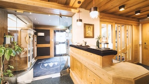 A wooden interior with a reception desk, a framed picture on the wall, and a glass door leading outside. - Lärchenhof - Premium Apartments & Zimmer (Sankt Anton am Arlberg)