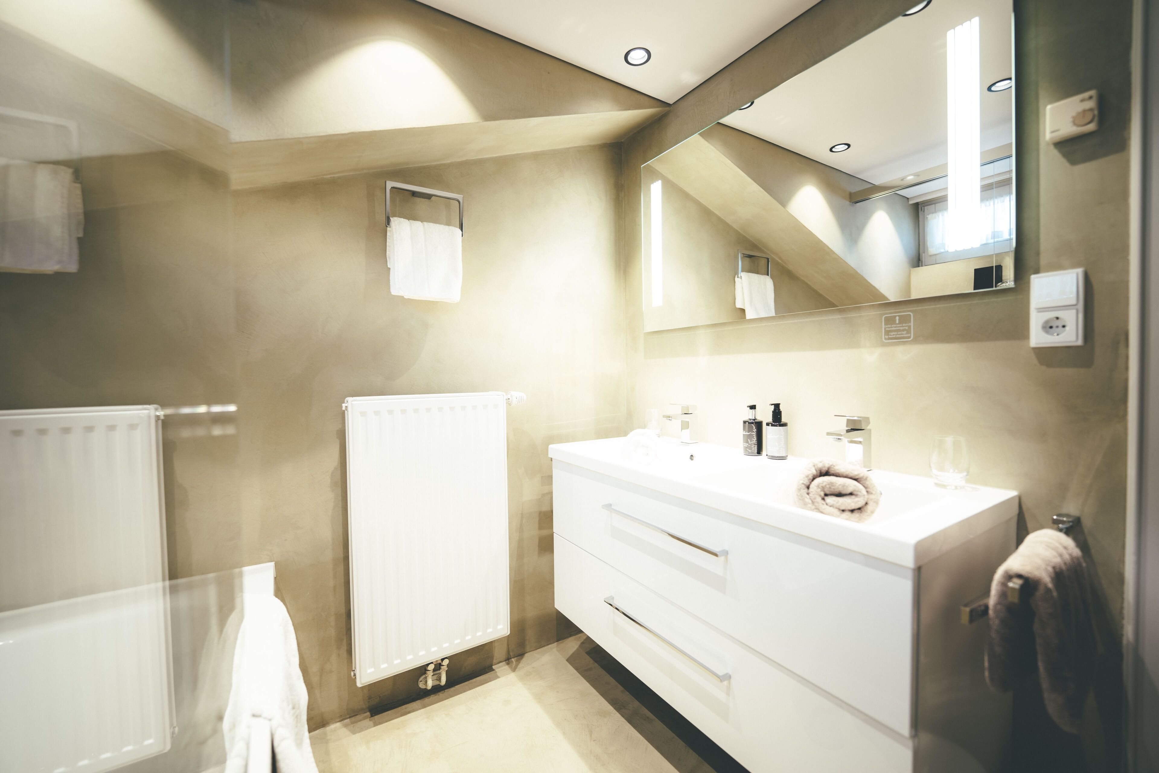 A modern bathroom with a white vanity, a large mirror, and a towel rack.