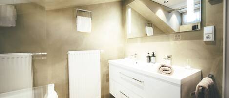 A modern bathroom with a white vanity, a large mirror, and a towel rack.