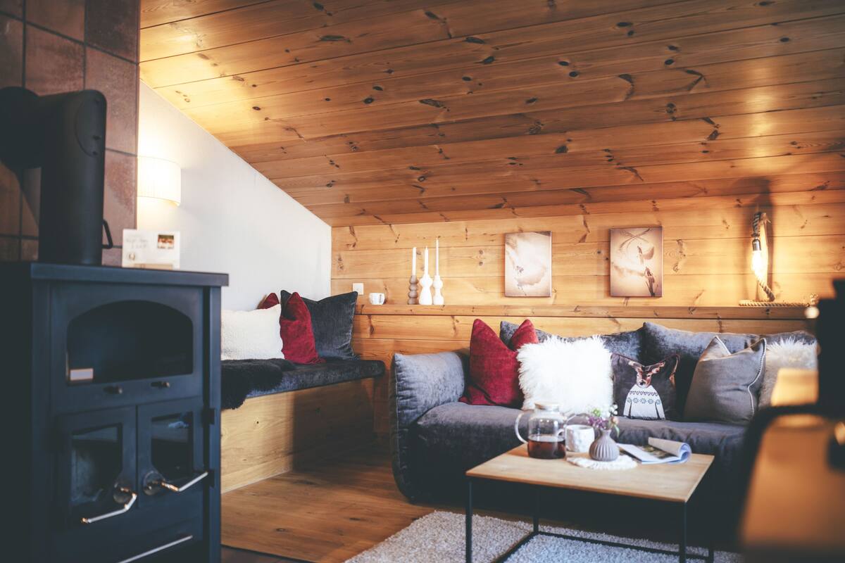 A cozy living room with a wooden ceiling, a fireplace, a sofa, and a coffee table.