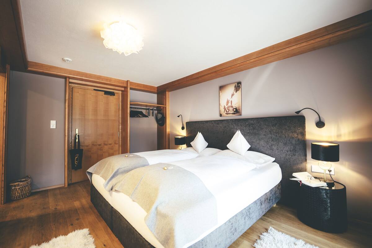 A bedroom with a large bed, wooden ceiling beams, a wardrobe, and a bedside table with a lamp.