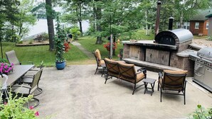 An outdoor patio with a grill, seating, and a view of a lake.