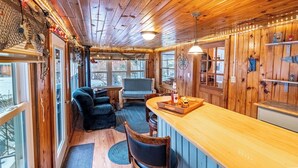 A cozy cabin interior with wooden walls, a bar area, and a seating space.
