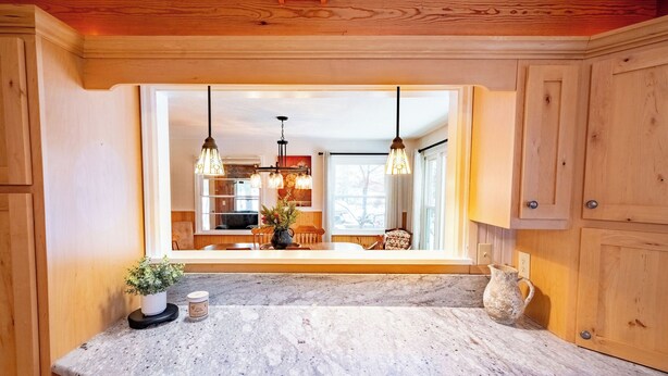 A kitchen with a marble countertop, wooden cabinets, and a large window overlooking the dining area.