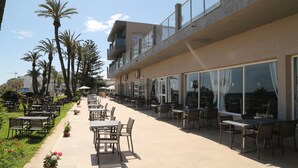 Un espacio de comedor al aire libre con mesas y sillas, un sendero y palmeras.