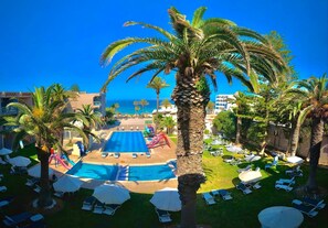 Un área de piscina con sillones de descanso, sombrillas y palmeras.