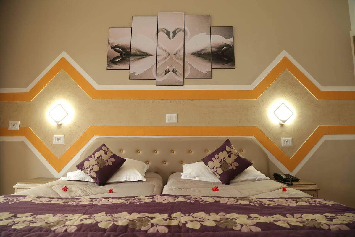 Une chambre d’hôtel comprenant un lit, deux tables de chevet, une œuvre d’art accrochée au mur et deux appliques murales.