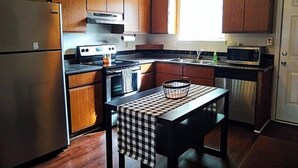 Cocina compacta con armarios de madera, refrigerador de acero inoxidable, estufa a gas, microondas y un lavamanos.