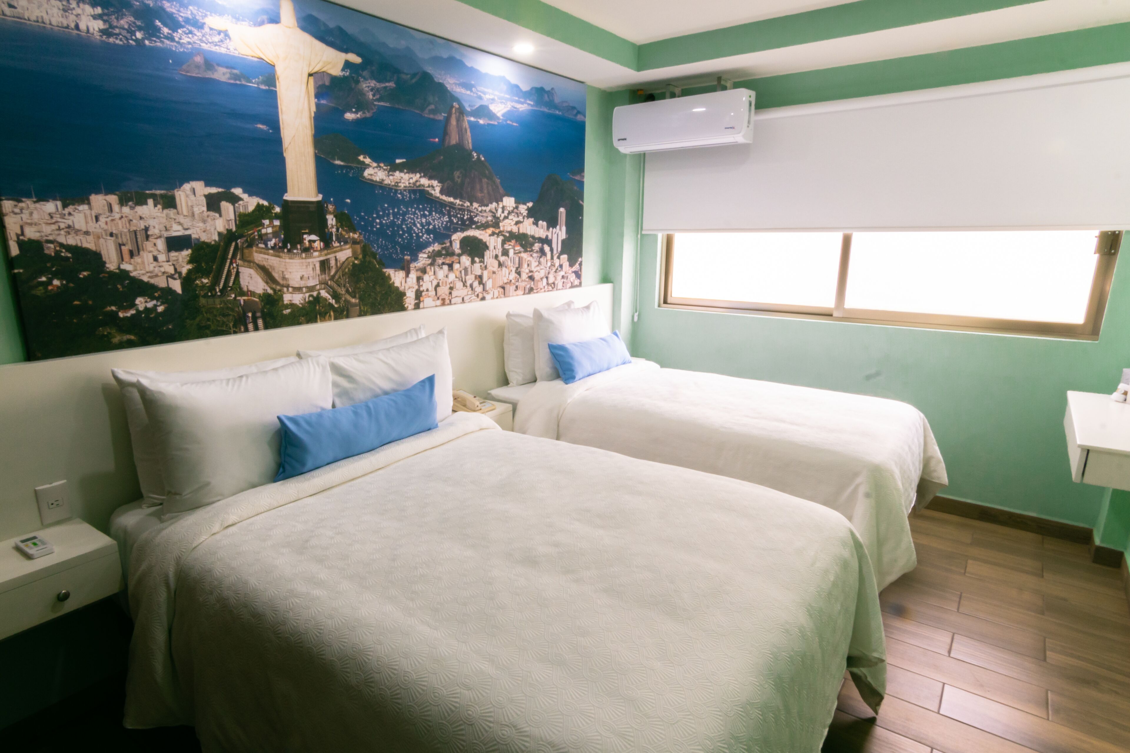 A hotel room with two beds, a mural of Christ the Redeemer, and a window with blinds.