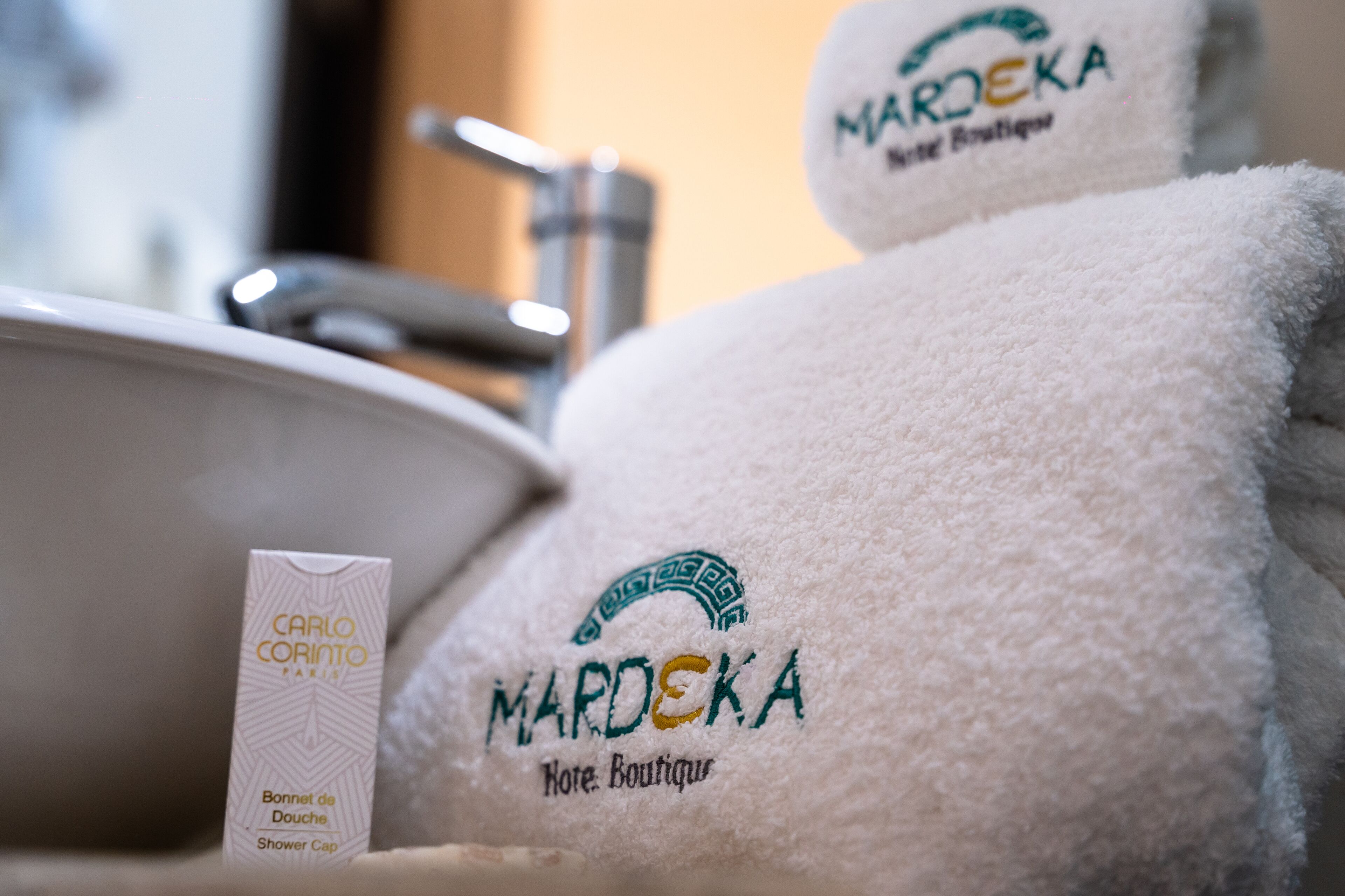 Un bagno con un lavandino, un berretto da doccia e due asciugamani con il logo 'Mardeka'.