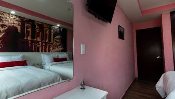 A hotel room with pink walls, a large bed with white bedding, a bedside table, a TV mounted on the wall, and a door leading to another room.