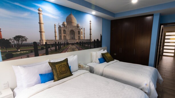 Camera d'albergo con due letti, un grande murale raffigurante il Taj Mahal e un armadio in legno.