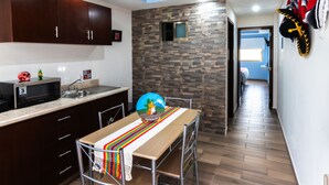 Una cucina con mobili in legno scuro, un forno a microonde e un lavandino. Si vede un tavolo con una tovaglia colorata e una sedia. È visibile anche un elemento decorativo a parete.