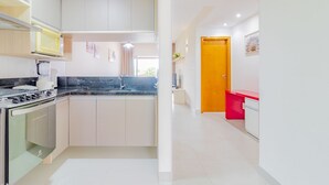 Een moderne keuken met een ingebouwde oven, een magnetron en een spoelbak. Een houten deur leidt naar een andere kamer.