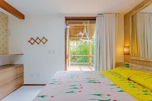A bedroom with a bed, a wooden dresser, a hanging light fixture, and a view of a balcony.
