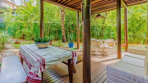 Pátio externo com mesa coberta por toalha, cercado por móveis de vime e vasos de plantas.