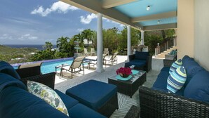 A covered outdoor seating area with a pool, lounge chairs, and a view of the ocean. - Villa Colada, a 4-Bedroom St. John Villa Above Rendezvous Bay (St. John)