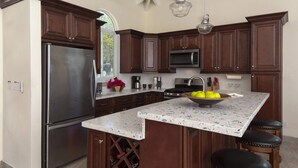 A kitchen with dark wood cabinets, a stainless steel refrigerator, a microwave, and a granite countertop. - Villa Colada, a 4-Bedroom St. John Villa Above Rendezvous Bay (St. John)