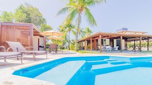 A swimming pool with lounge chairs and umbrellas, surrounded by wooden structures and palm trees. - GB69 Excellent 4/4 house 400m from the beach (Camaçari)