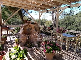 Un espacio al aire libre techado con una estructura de piedra, sillas de madera y plantas en macetas.
