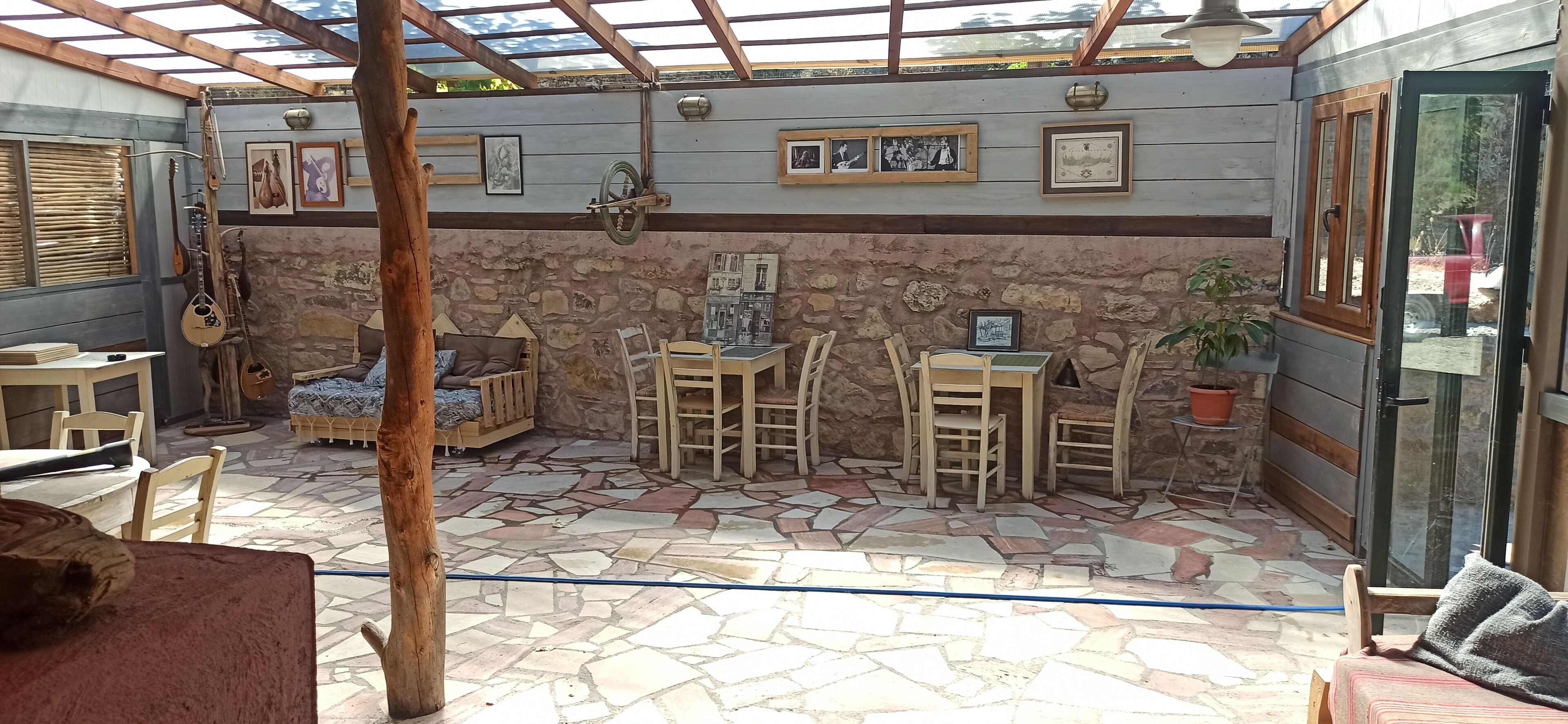 A covered patio with stone flooring, wooden furniture, and framed pictures on the walls.
