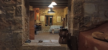 A rustic stone interior with a wooden door, a hanging light fixture, and a stone fireplace.