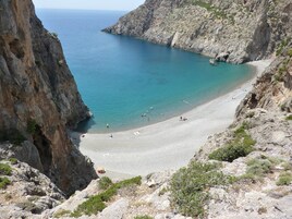 A coastal beach with rocky cliffs and clear blue waters.