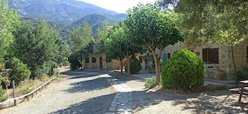 A stone building with a courtyard, surrounded by trees and a mountain backdrop.
