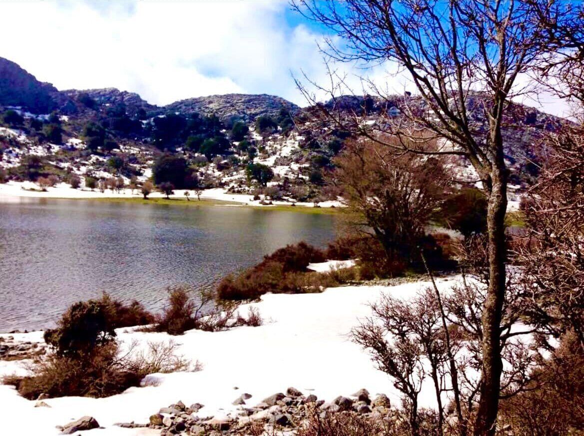 Un lago rodeado de colinas nevadas y vegetación escasa.