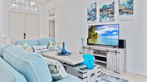 A living room with a large flat-screen TV, a light blue sofa, and a wooden entertainment unit. - Waterfront Home with Pool,  Hot Tub, Dock, Game Room & 10 minutes to the Beach (Palm Coast)