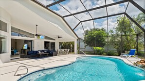 A modern indoor pool with a glass ceiling, a seating area with a sofa and chairs, and a view of the surrounding greenery. - Waterfront Home with Pool,  Hot Tub, Dock, Game Room & 10 minutes to the Beach (Palm Coast)
