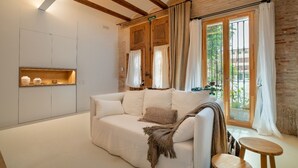 A cozy room with a white sofa, a small wooden table, and a window with curtains. - Design house with swimming pool near the beach (València)