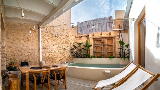 A cozy outdoor seating area with a wooden table and chairs, a hammock, and a stone wall backdrop. - Design house with swimming pool near the beach (València)