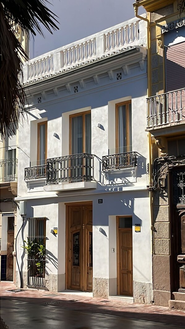 A two-story building with a white facade, wooden doors, and balconies with wrought iron railings. - Design house with swimming pool near the beach (València)