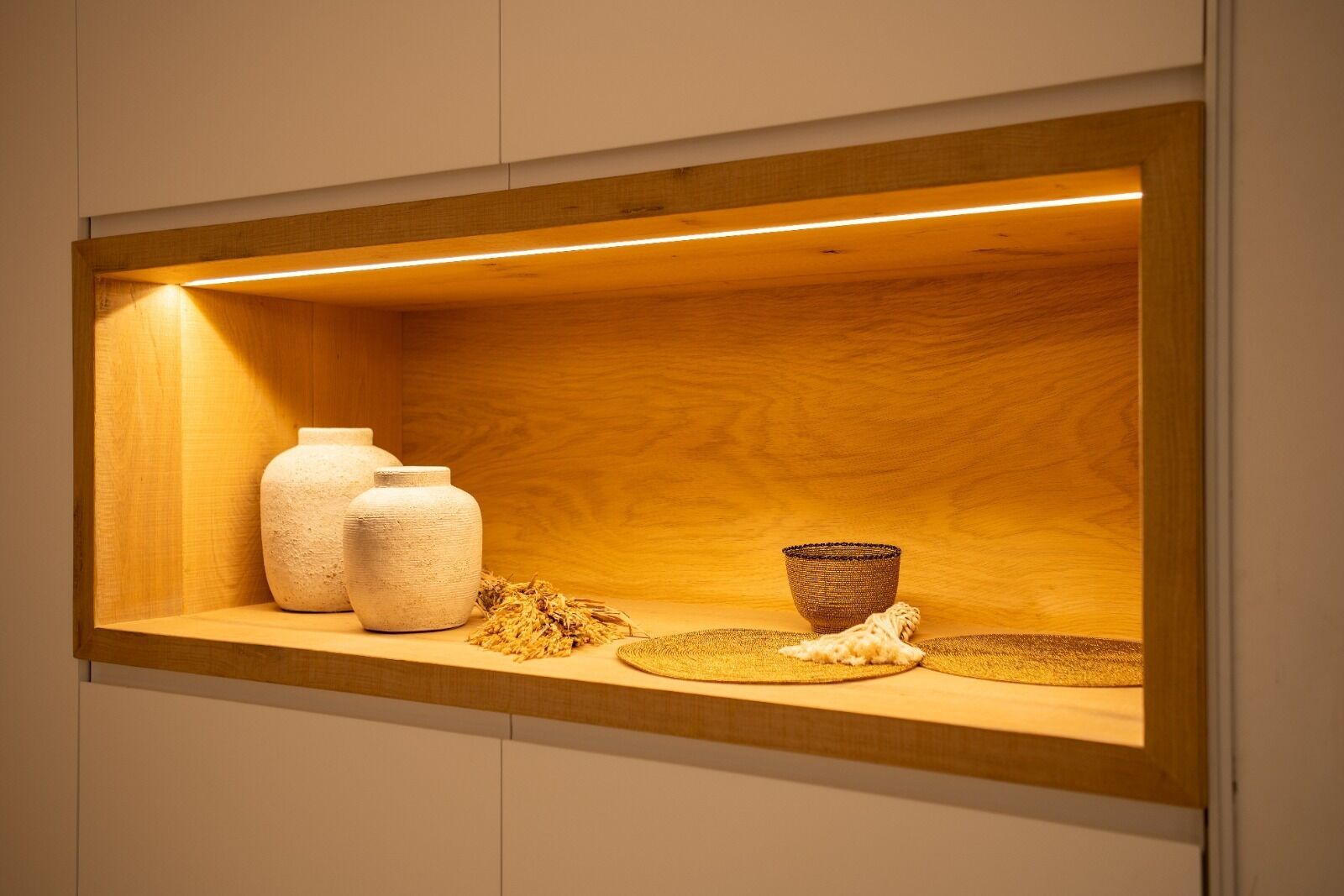 Un estante de madera con tres frascos de cerámica y una cesta tejida frente a una pared de madera.
