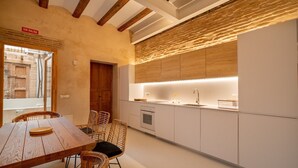 A modern kitchen with white cabinets, a wooden dining table, wicker chairs, and a view of the street outside. - Design house with swimming pool near the beach (València)