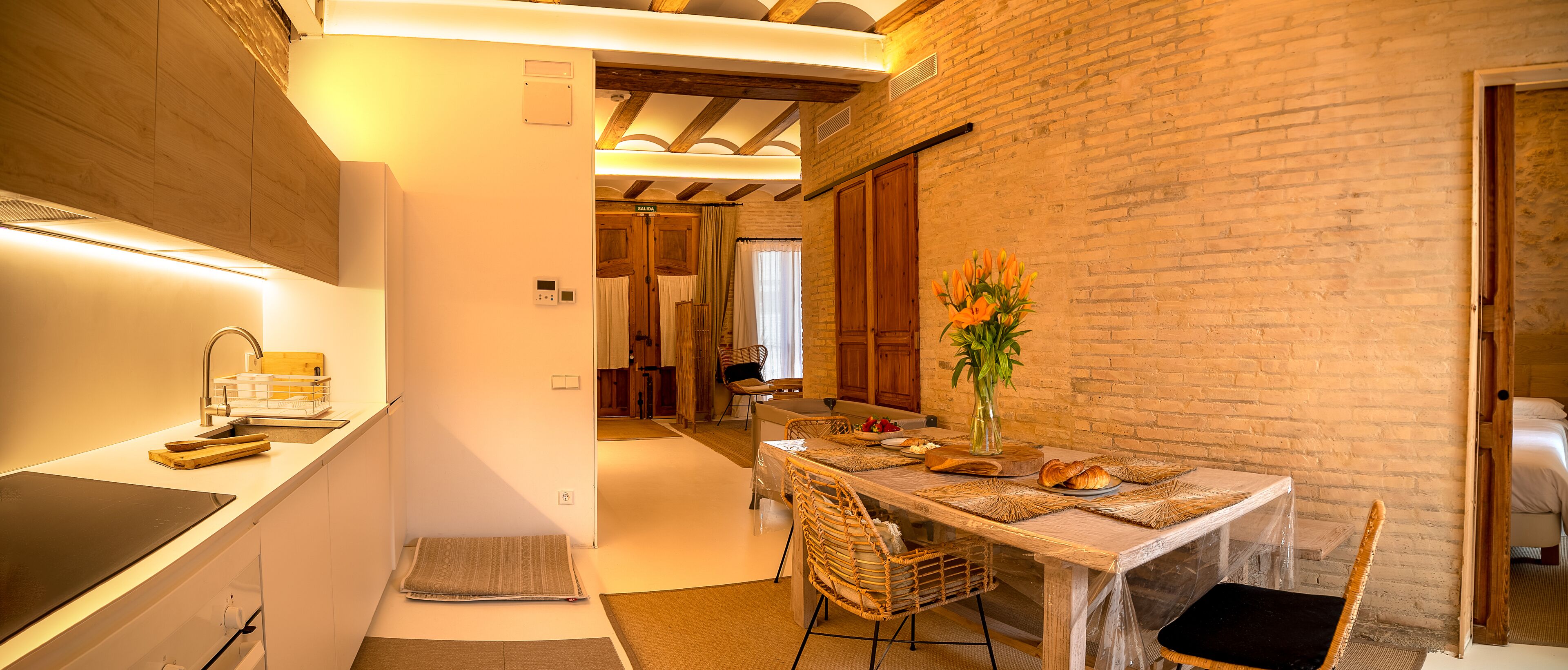 A modern kitchen with a built-in stove, a dining area with a table set for two, and a brick wall.