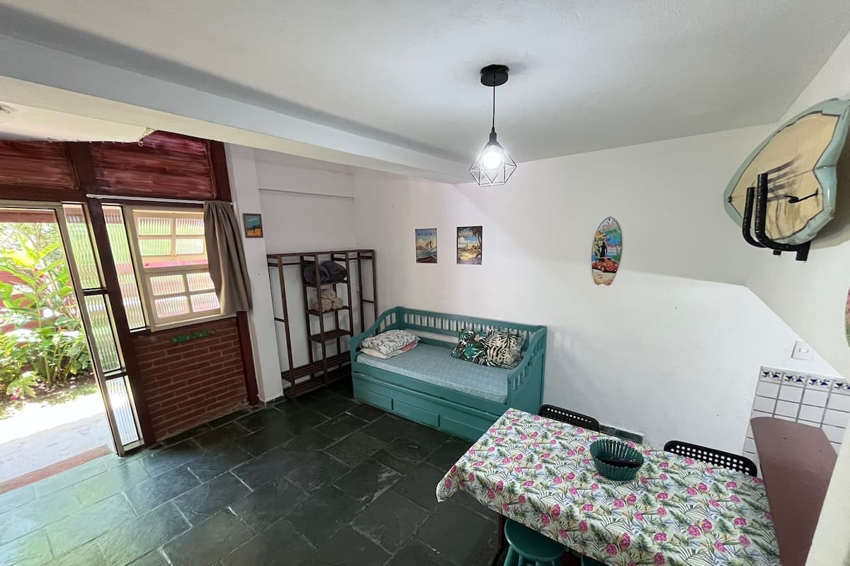 Een compacte kamer met een bed, een tafel met stoelen, een hanglamp en een klein raam.
