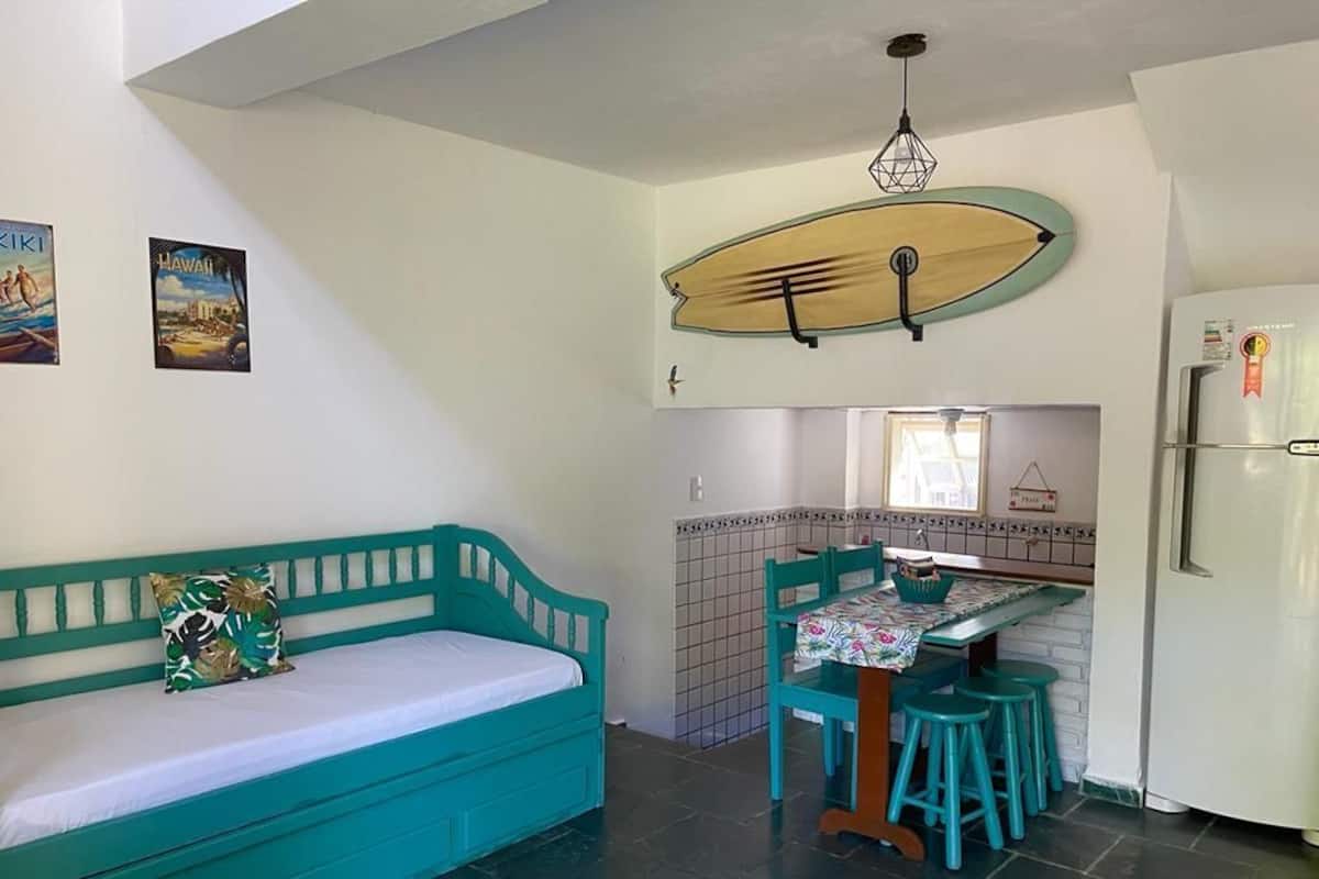 Een kleine keuken met een eethoek, een blauwgroene bank en een surfboard decoratie.