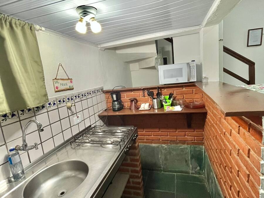 A compact kitchen with a stainless steel sink, a microwave, and a brick backsplash.