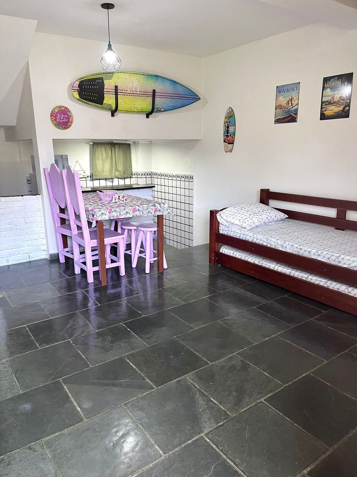 Quarto com área de jantar, mesa e cadeiras, uma cama e uma decoração de prancha de surf na parede.